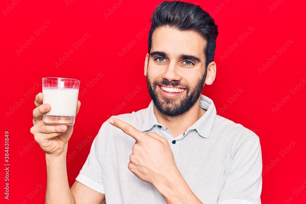 Young handsome man with beard drinking glass of milk smiling happy pointing with hand and finger Young handsome man with beard drinking glass of milk smiling happy pointing with hand and finger