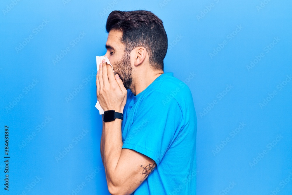 Young hispanic man illness using paper handkerchief on nose. Standing over isoltated blue background Young hispanic man illness using paper handkerchief on nose. Standing over isoltated blue background