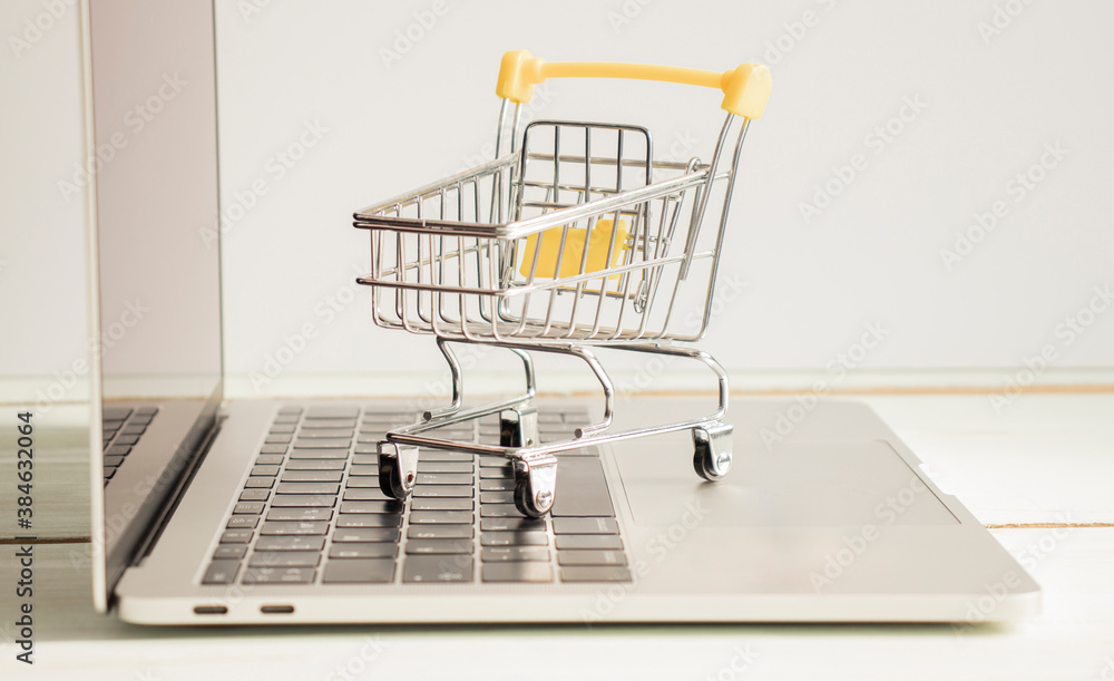 Small shopping trolley standing on the laptop close-up. Online shopping, e-commerce concept.