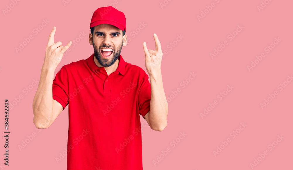 Young handsome man with beard wearing delivery uniform shouting with crazy expression doing rock symbol with hands up. music star. heavy music concept. Young handsome man with beard wearing delivery uniform shouting with crazy expression doing rock symbol with hands up. music star. heavy music concept.