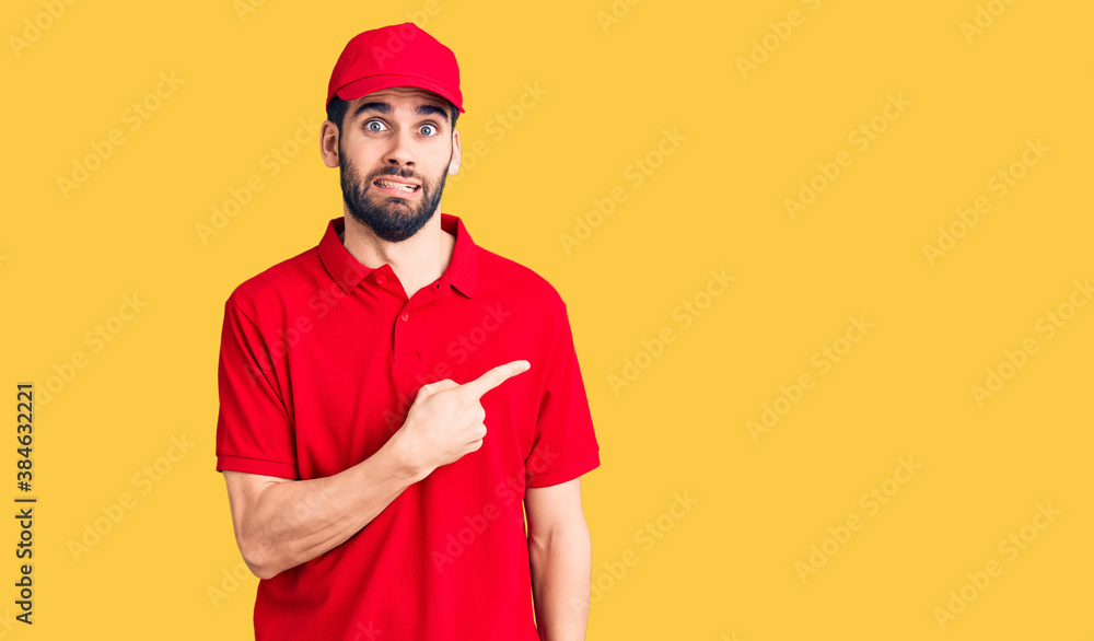 Young handsome man with beard wearing delivery uniform pointing aside worried and nervous with forefinger, concerned and surprised expression