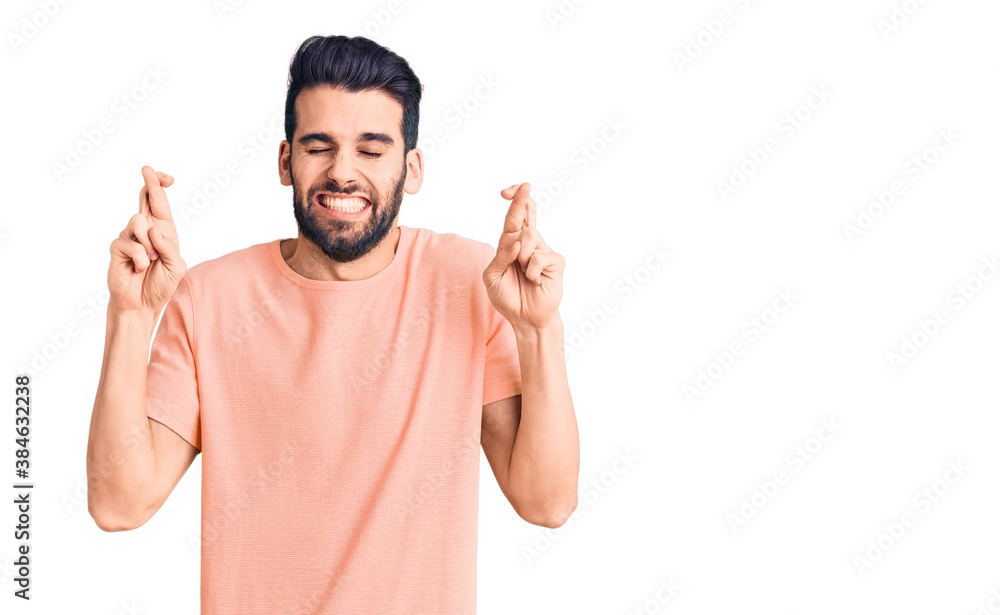 Young handsome man with beard wearing casual t-shirt gesturing finger crossed smiling with hope and eyes closed. luck and superstitious concept. Young handsome man with beard wearing casual t-shirt gesturing finger crossed smiling with hope and eyes closed. luck and superstitious concept.
