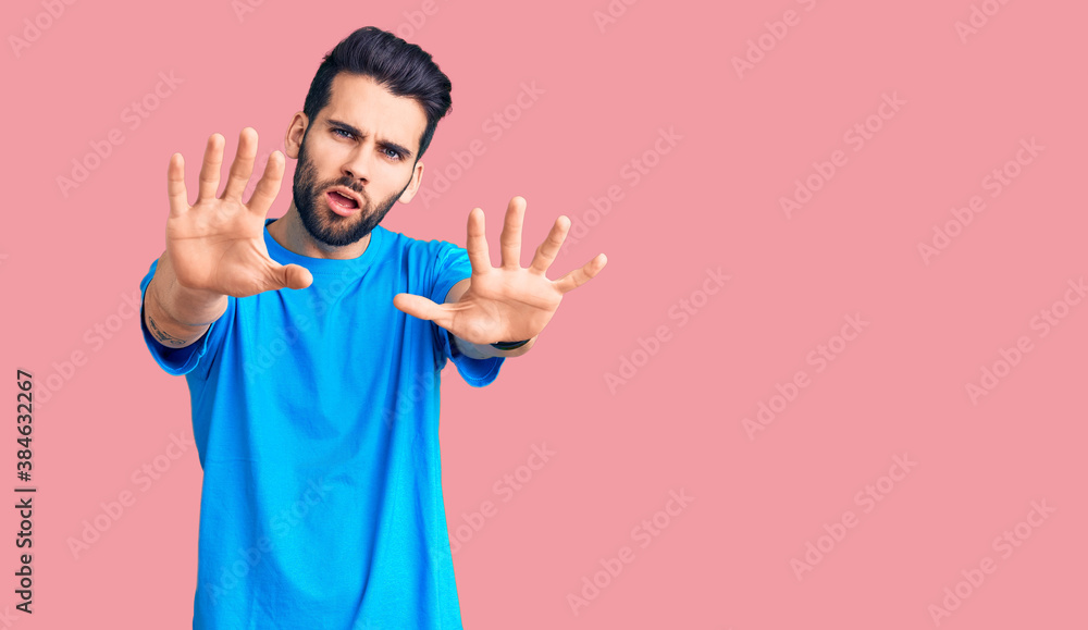 Young handsome man with beard wearing casual t-shirt doing stop gesture with hands palms, angry and frustration expression