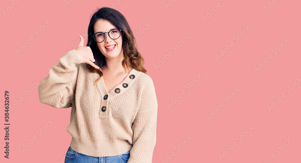 Beautiful young brunette woman wearing casual clothes and glasses smiling doing phone gesture with hand and fingers like talking on the telephone. communicating concepts. Beautiful young brunette woman wearing casual clothes and glasses smiling doing phone gesture with hand and fingers like talking on the telephone. communicating concepts.