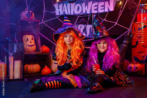 Two Little beautiful girls in a witch costumes celebrates Happy Halloween party in interior with pumpkins.