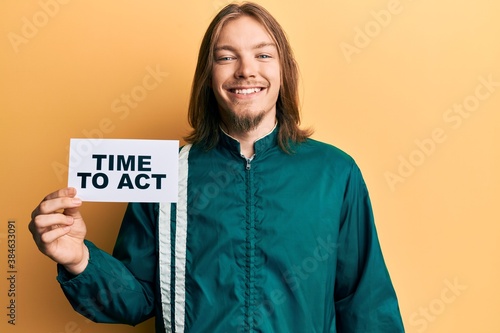 Handsome caucasian man with long hair holding time to act banner looking positive and happy standing and smiling with a confident smile showing teeth