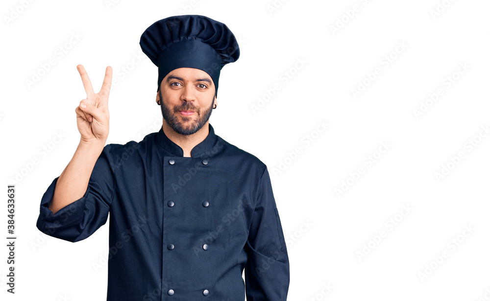 Young hispanic man wearing cooker uniform showing and pointing up with fingers number two while smiling confident and happy. Young hispanic man wearing cooker uniform showing and pointing up with fingers number two while smiling confident and happy.