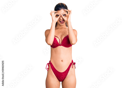 Young beautiful woman wearing bikini doing ok gesture like binoculars sticking tongue out, eyes looking through fingers. crazy expression. © Krakenimages.com