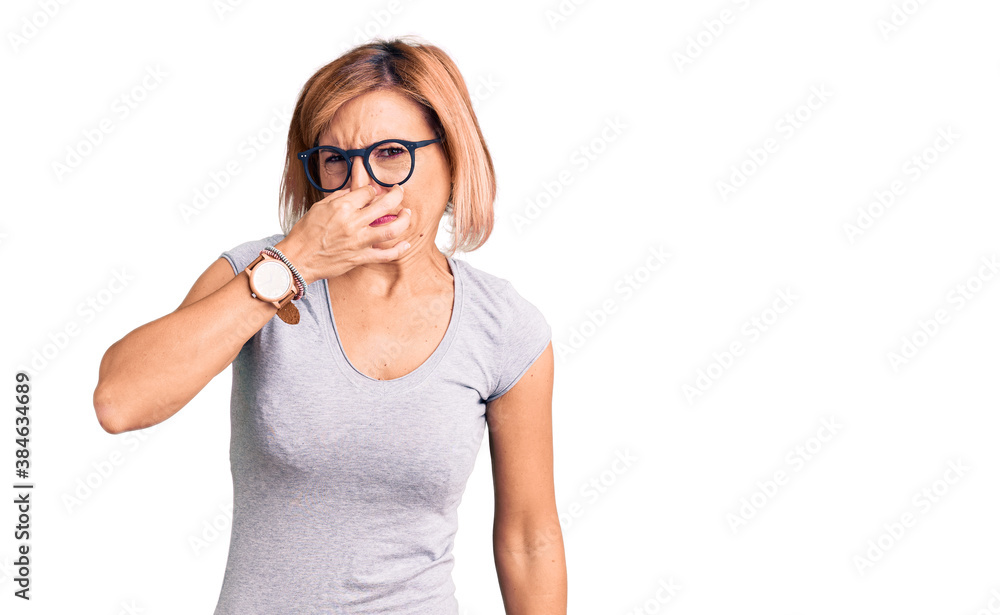 Young blonde woman wearing casual clothes smelling something stinky and disgusting, intolerable smell, holding breath with fingers on nose. bad smell