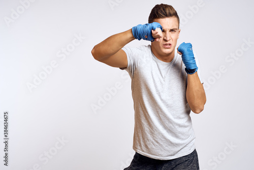 sporty male boxer in blue gloves practicing punches on a light background cropped view