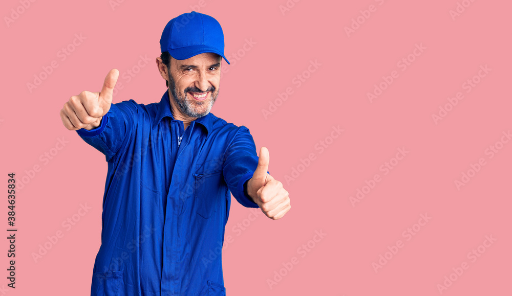 Middle age handsome man wearing mechanic uniform approving doing positive gesture with hand, thumbs up smiling and happy for success. winner gesture.