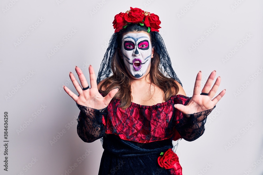 Young woman wearing day of the dead costume over white afraid and terrified with fear expression stop gesture with hands, shouting in shock. panic concept. Young woman wearing day of the dead costume over white afraid and terrified with fear expression stop gesture with hands, shouting in shock. panic concept.