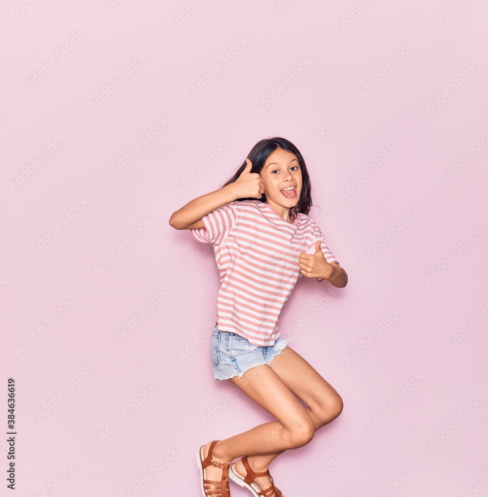 Adorable hispanic child girl wearing casual clothes smiling happy. Jumping with smile on face doing ok sign with thumbs up over isolated pink background Adorable hispanic child girl wearing casual clothes smiling happy. Jumping with smile on face doing ok sign with thumbs up over isolated pink background