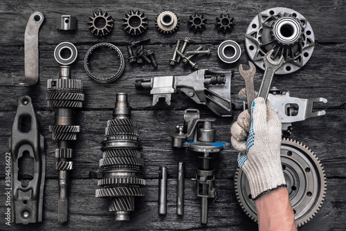 Disassembled parts of a car gearbox and an auto mechanic with a wrench in hand. photo