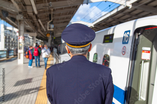 Shinkansen Nozomi Bullet train conductor checks the platform as the train is getting ready to leave, back portrait, no face, elderly man in a uniform