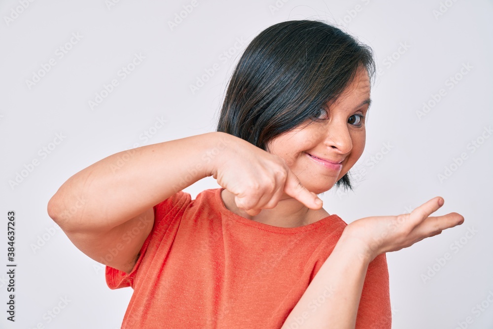 Brunette woman with down syndrome wearing casual clothes amazed and smiling to the camera while presenting with hand and pointing with finger. Brunette woman with down syndrome wearing casual clothes amazed and smiling to the camera while presenting with hand and pointing with finger.