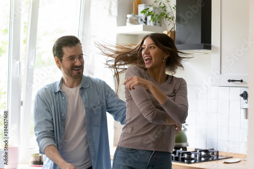 Emotional playful young family couple dancing in modern kitchen. Energetic millennial handsome man twisting attractive laughing beloved woman, involved in funny domestic activity together indoors.