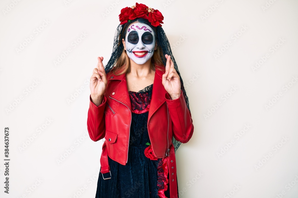 Woman wearing day of the dead costume over white gesturing finger crossed smiling with hope and eyes closed. luck and superstitious concept. Woman wearing day of the dead costume over white gesturing finger crossed smiling with hope and eyes closed. luck and superstitious concept.