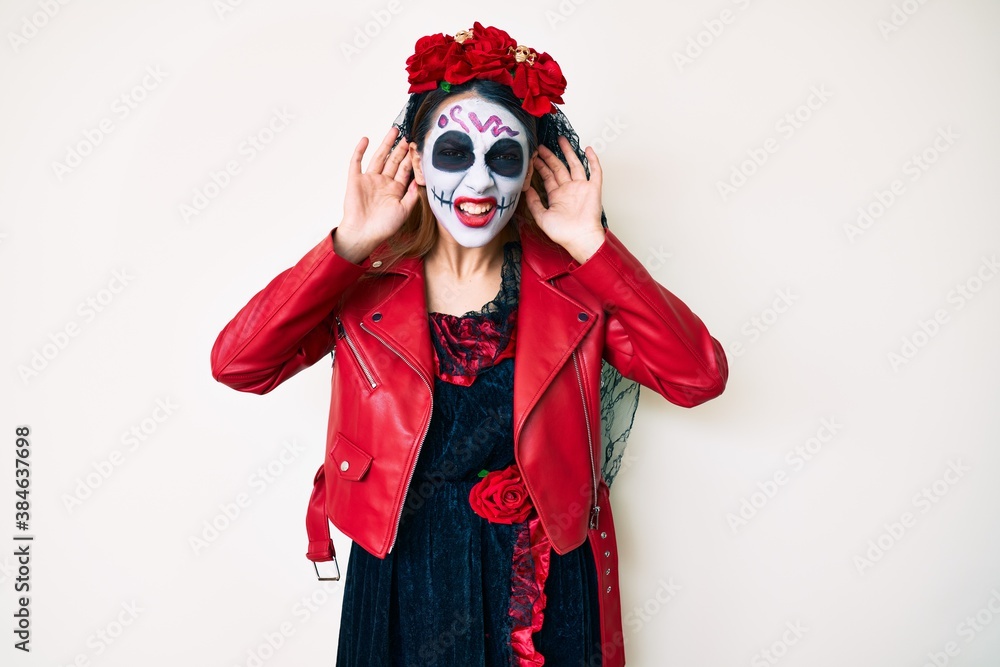 Woman wearing day of the dead costume over white trying to hear both hands on ear gesture, curious for gossip. hearing problem, deaf Woman wearing day of the dead costume over white trying to hear both hands on ear gesture, curious for gossip. hearing problem, deaf