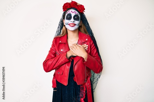 Woman wearing day of the dead costume over white smiling with hands on chest with closed eyes and grateful gesture on face. health concept.