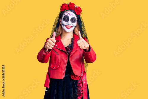 Woman wearing day of the dead costume over background approving doing positive gesture with hand, thumbs up smiling and happy for success. winner gesture.