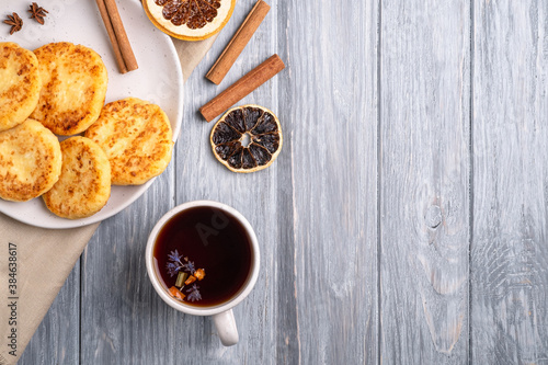 Cottage cheese fritters with hot black aromatic tea, Christmas breakfast mood with anise, cinnamon and dried citrus on wooden background, top view