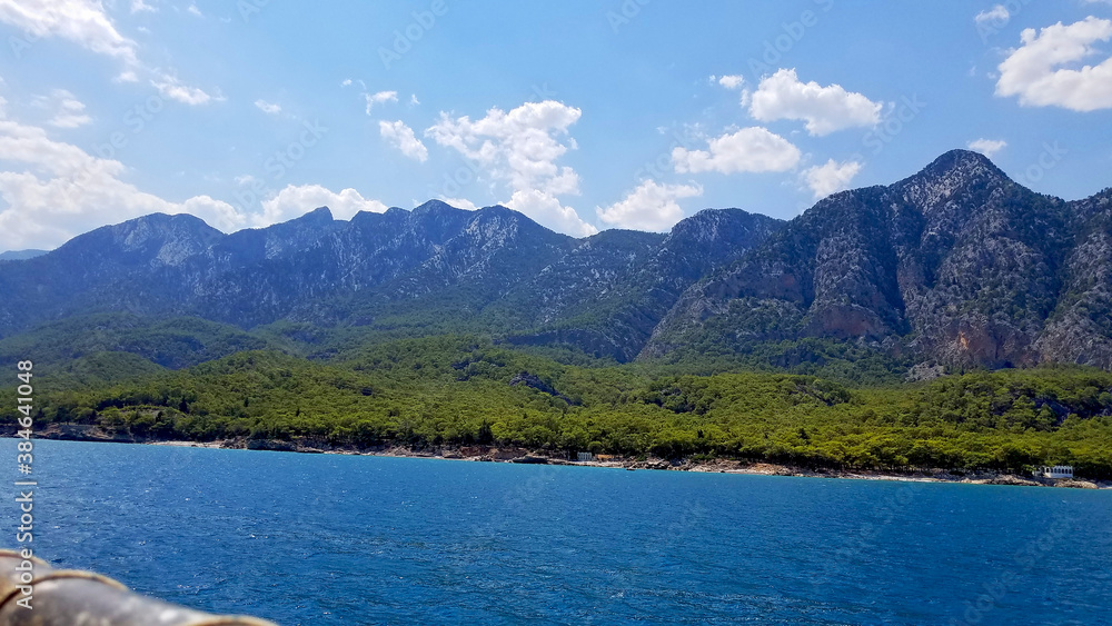 blue sea, coastline and mountains overgrown with forest under a blue sky with white clouds