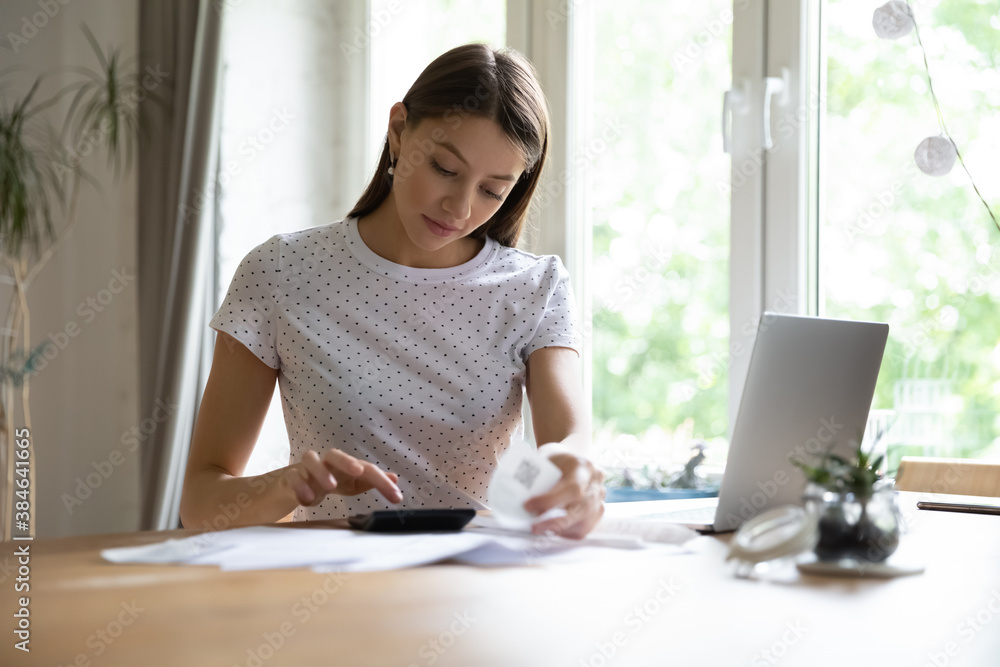 Focused young pretty woman sitting at home office, calculating monthly expenses or checking bills at home. Concentrated millennial lady planning household budget or paying taxes invoices indoors. Focused young pretty woman sitting at home office, calculating monthly expenses or checking bills at home. Concentrated millennial lady planning household budget or paying taxes invoices indoors.