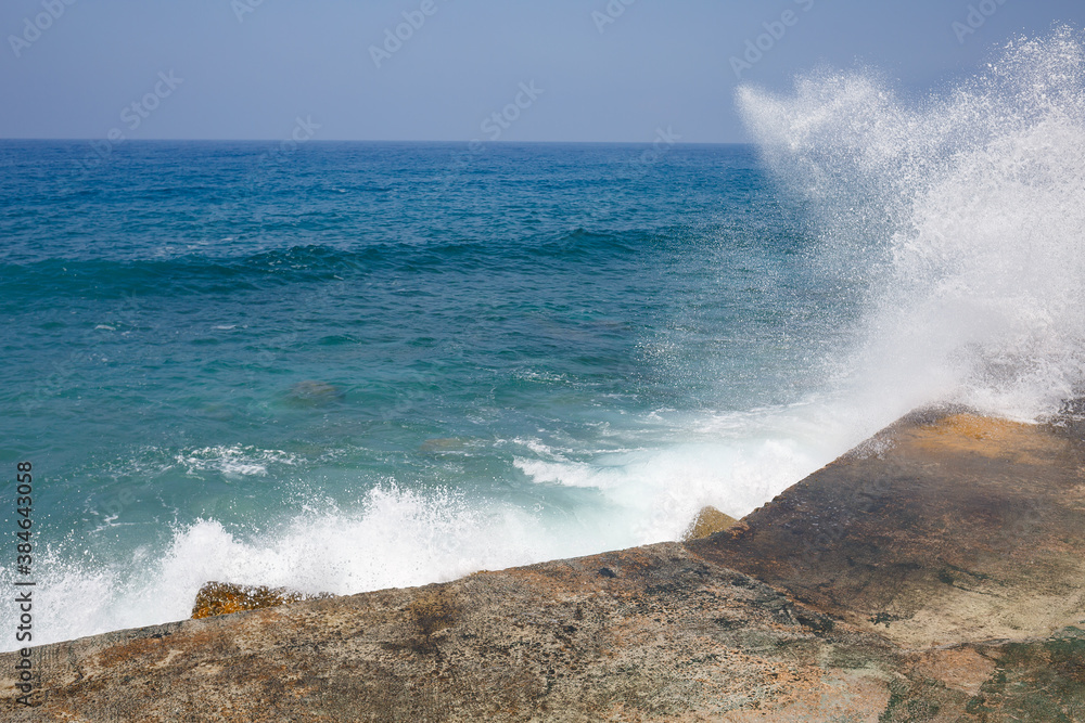Sea water beats against rocky rocks and makes waves with foam