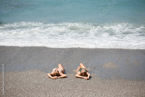 Two girls girlfriend are sitting on the sea sandy shore and the waves soaked them in bathing suits on a sunny warm day