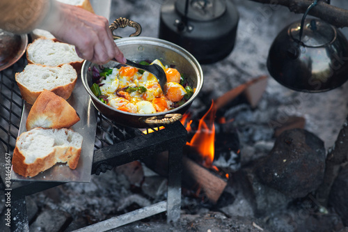 Detail view of camp fire cooking, breads are in a row, a tea pot and onion pan is on the fire with copy space