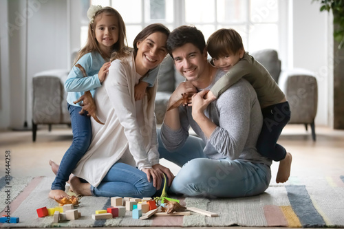 Portrait of happy young Caucasian family with small kids sit on floor in living room have fun on weekend together. Smiling parents with little children play at home. Tenancy  relocation concept.