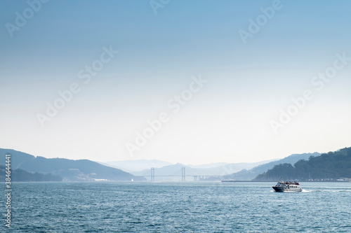 View of the Ría de Vigo from the inside, with the Rande Bridge in the background and a ferry sailing through it in a lightly misty day, copy space up