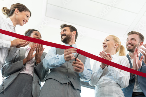 Businessman cutting red ribbon with colleagues at office photo