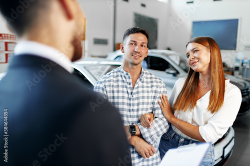 Man car salesman telling about the features of the new car to the couple