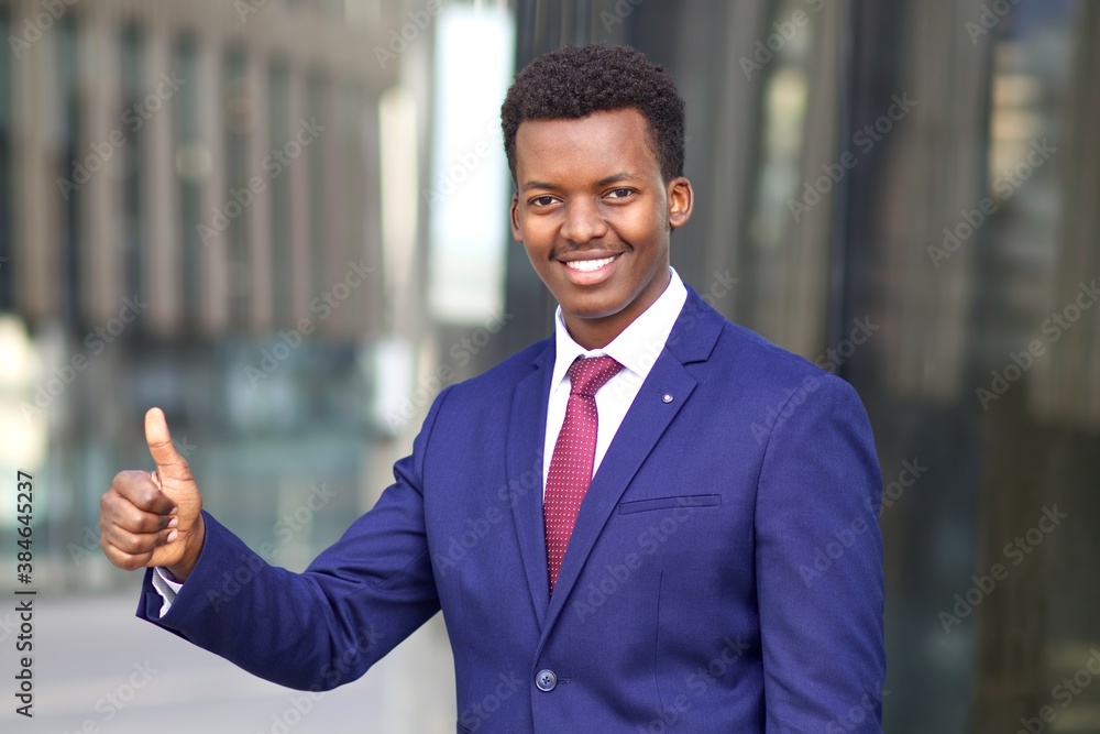 Portrait of happy positive man, black African Afro American young businessman in formal suit with tie smiling wide, looking at camera, showing thumb up, like gesture. Business concept. Portrait of happy positive man, black African Afro American young businessman in formal suit with tie smiling wide, looking at camera, showing thumb up, like gesture. Business concept.