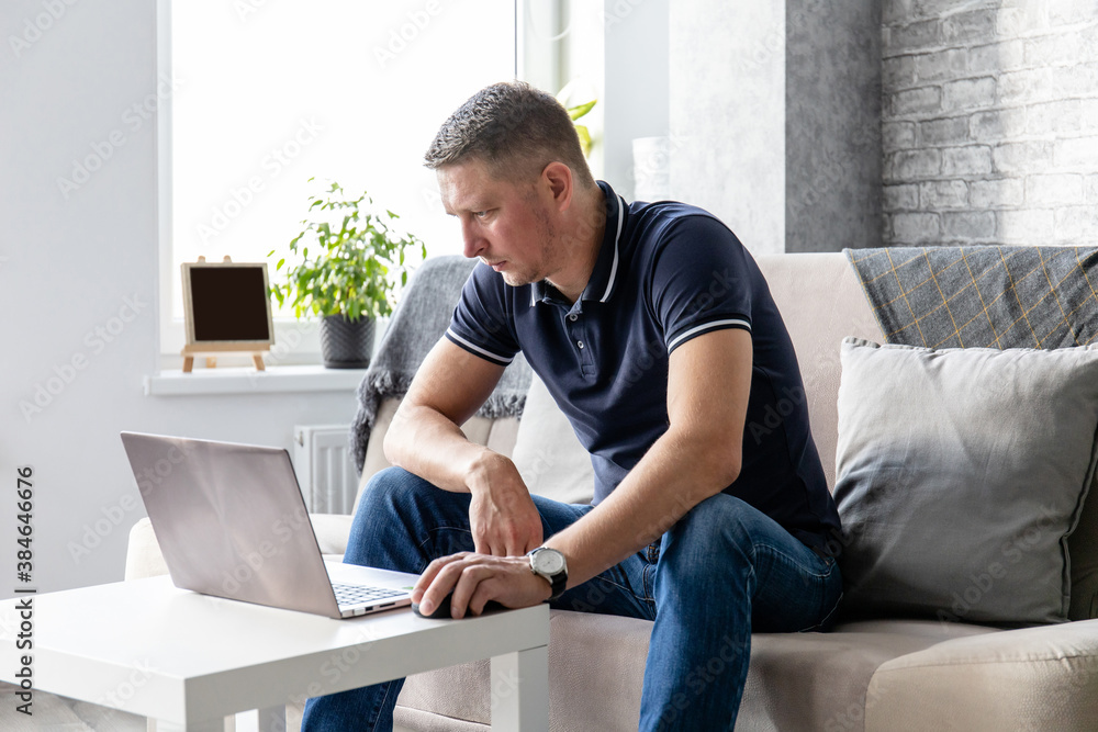 a man works at a laptop while sitting on the couch in a bright room a man works at a laptop while sitting on the couch in a bright room