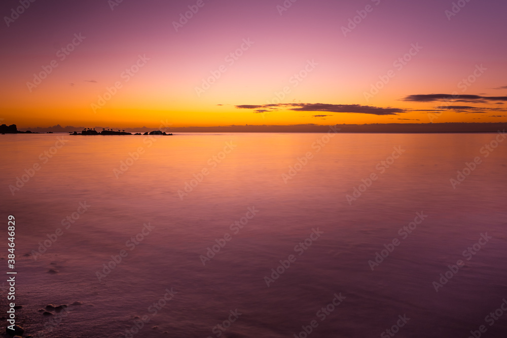 Vivid purple glowing sunset over smooth water and rock bird silhouettes