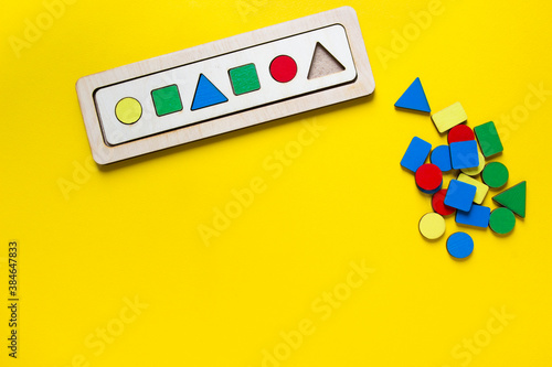 on a yellow background, there is a children's wooden toy sorter for studying shapes and colors