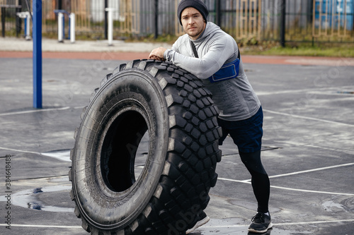 Athletic man leans on the tire and rests. Sports field, tire turning, full body exercises