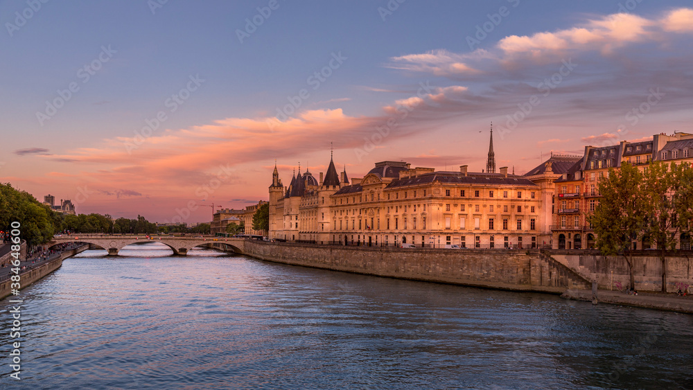 Paris, France - August 28, 2020: View of Seine river with Conciergerie palace, bridge over the Seine river and Parisians walking on the embankment at sunset