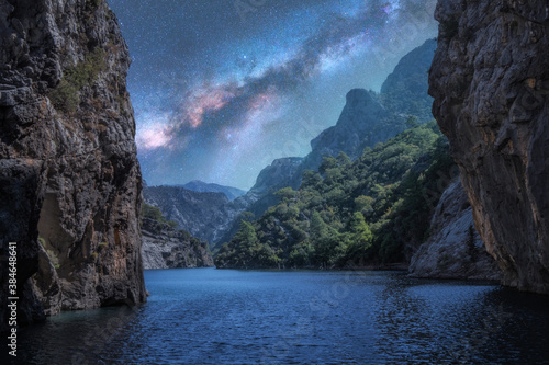 Milky Way over the beautiful mountain canyon and blue sea at night in summer. Colorful landscape with bright starry sky with Milky Way, rocks, trees, moonlight, constellation. Galaxy. Nature and space