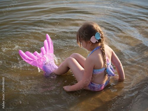 Dziewczynka przebrana za syrenkę siedzi na brzegu jeziora