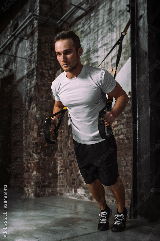 Full body determined male athlete doing chest press exercise on TRX ropes during functional fitness workout in grungy gym Full body determined male athlete doing chest press exercise on TRX ropes during functional fitness workout in grungy gym