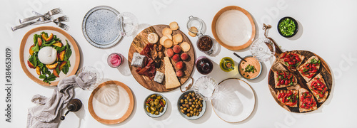 Family wine and snack party. Flay-lay of wineglases, boards with cheese, fruit, smoked meat, tomato brushettas, buratta salad over white table background, top view. Wine tasting, celebration concept