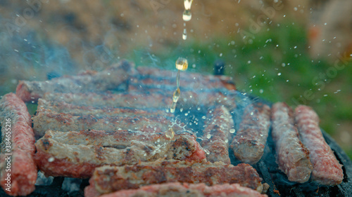 CLOSE UP: Person cooking meatrolls on the grill splashes them with cold beer. photo