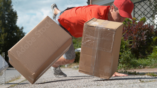 CLOSE UP: Courier trips and falls to asphalt pavement along with a few parcels. photo