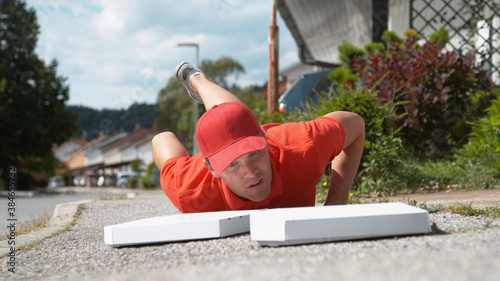 Photography CLOSE UP: Uncoordinated delivery man falls to the ground and drops two pizzas