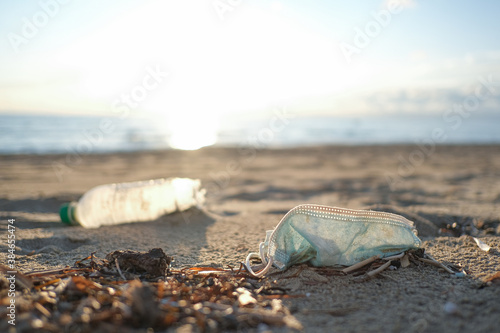 Medical face mask and plastic bottle discarded on dirty sea coast,covid19 pandemic disease pollution effects