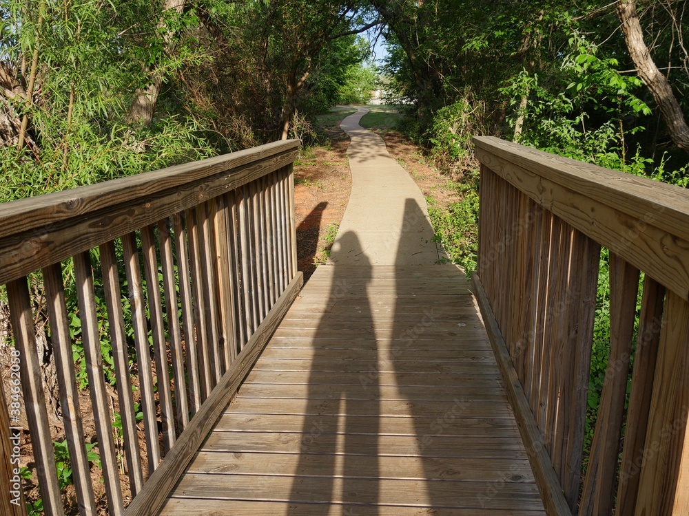 Close up of a wooden footbridge in a forest park with shadows of people